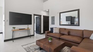 A modern living room with a sectional sofa, a coffee table, a TV mounted on the wall, and a console table with a plant. - Vizcaya #2 - Moab's Newest Luxury Rental (Hot Tub) (Moab)