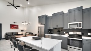 A modern kitchen with grey cabinets, a central island with bar stools, a built-in oven, and a microwave.