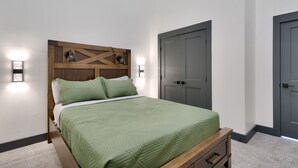 Quarto com cabeceira de madeira, colcha verde acolchoada, duas luminárias de mesa e porta cinza.