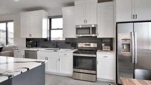 A modern kitchen with white cabinets, stainless steel appliances, and a large island. - Vizcaya #8 - Moab's Newest Luxury Rental (Moab)