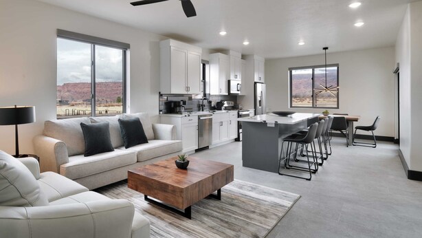 A modern kitchen with white cabinets, a central island, and a dining area with bar stools. - Vizcaya #8 - Moab's Newest Luxury Rental (Moab)