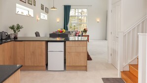 A modern kitchen with a central island, wooden cabinets, a built-in refrigerator, and a dining area with a view through a large window. - Narracott Down (South Molton)