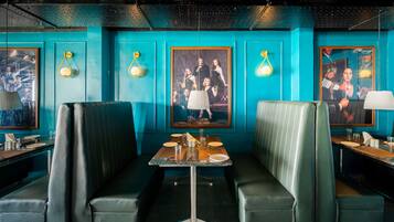 Um restaurante com paredes verde-água, assentos em verde e quadros decorativos nas paredes.