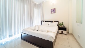 A modern hotel room with a large bed, a bedside table with a lamp, a mirror, and a window with curtains. - Rolling space (Puducherry)