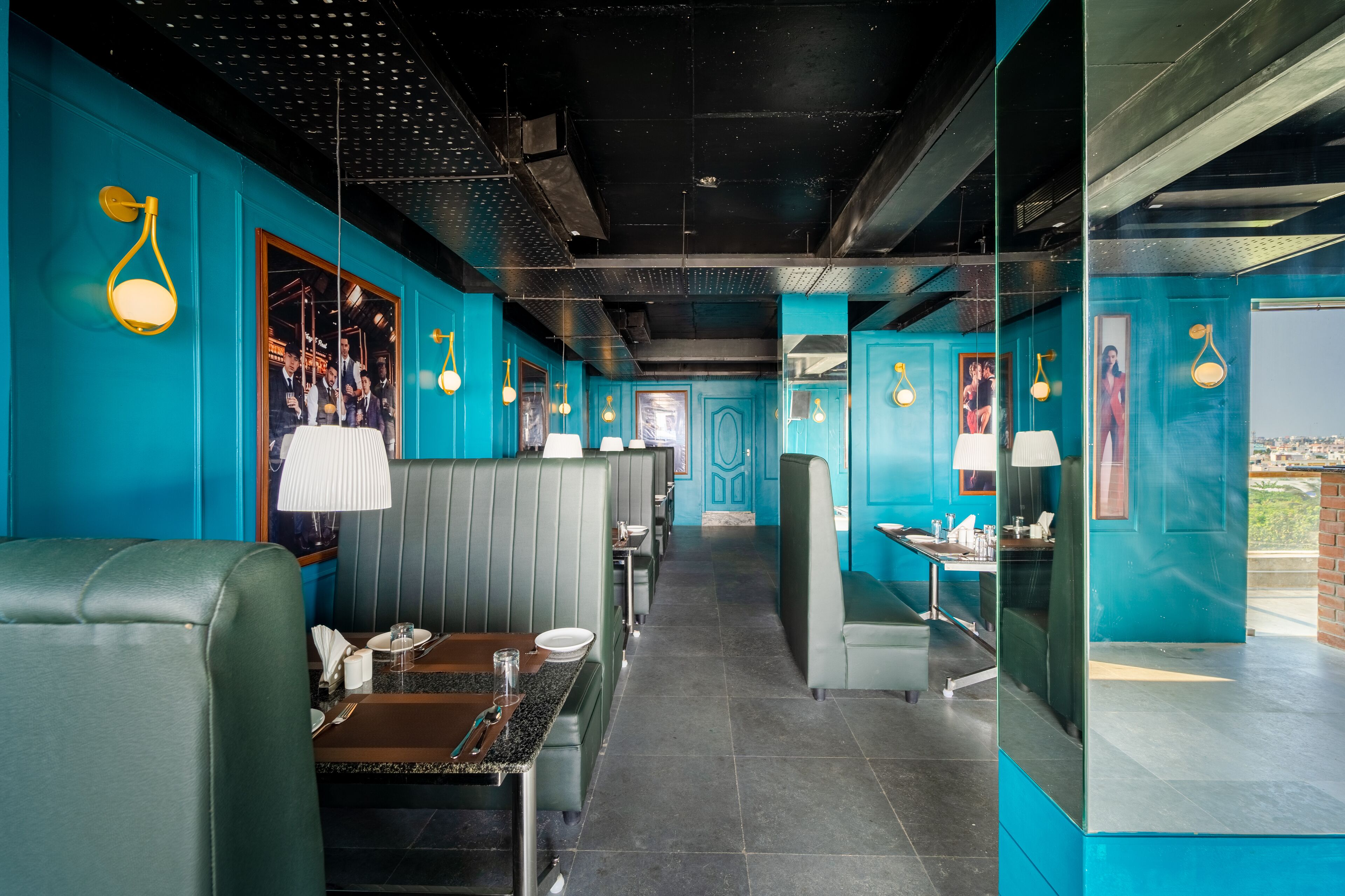 A restaurant with teal walls, black ceiling, and green seating. Tables are set with white tablecloths and lamps.