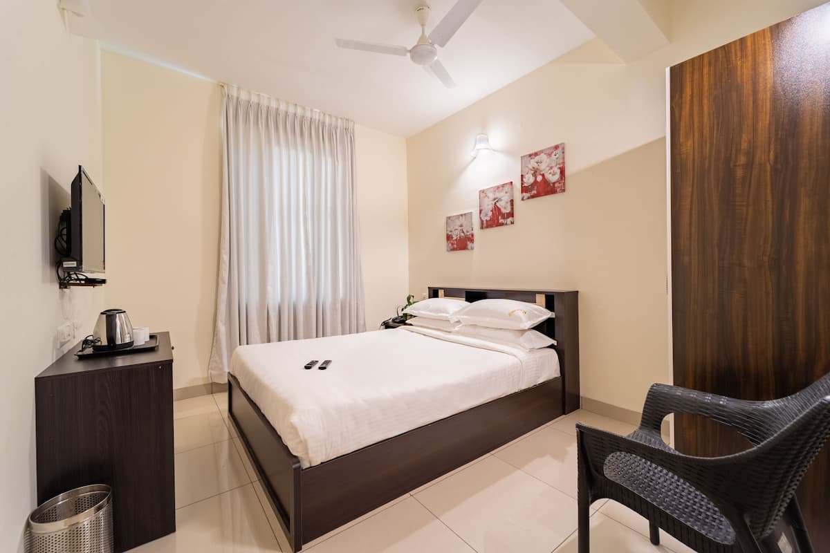 A hotel room with a bed, a desk, a chair, a ceiling fan, and artwork on the wall.