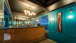 A bar area with a brick counter, shelves of bottles, and a city view through the window. - Rolling space (Puducherry)
