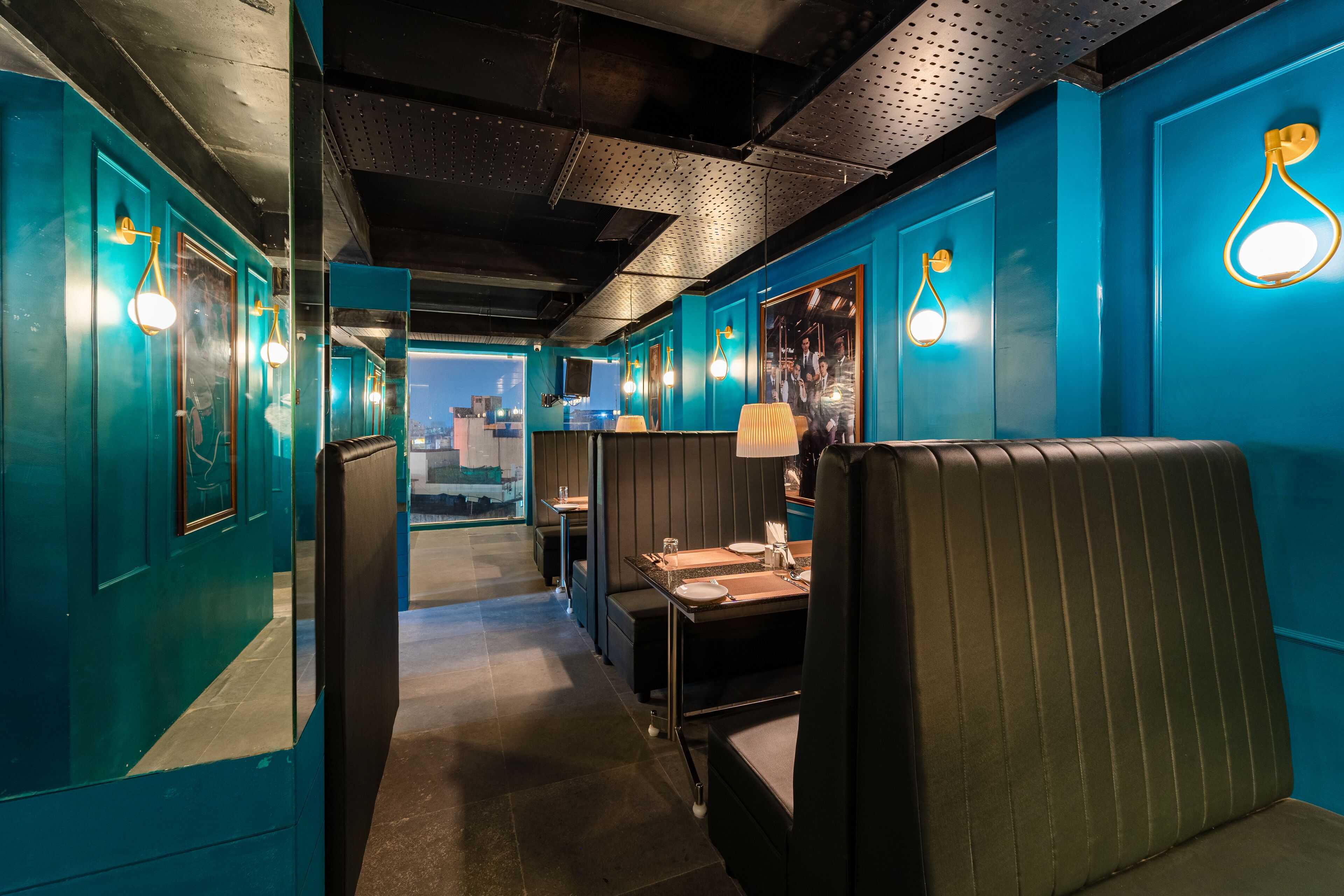Un restaurante con paredes verde azulado, cabinas negras e iluminación colgante.
