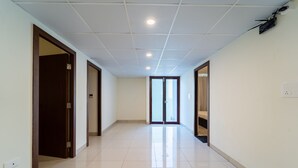 A corridor with a tiled floor, wooden doors, and a ceiling with recessed lighting. - Rolling space (Puducherry)