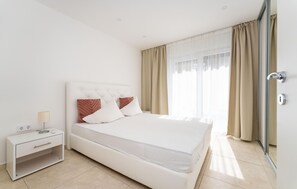 A modern hotel room with a bed, bedside table, lamp, and a view of the outside through the window.