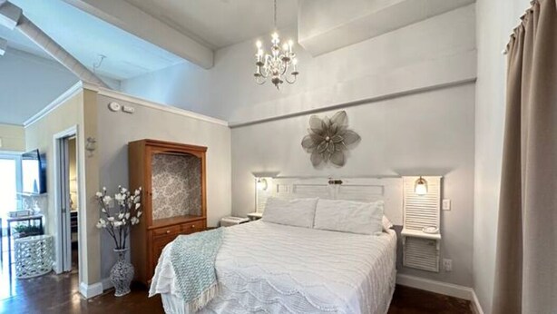 A bedroom with a large bed, a chandelier, a decorative wall piece, and a wooden cabinet. - Haven at Hazel~Downtown Bungalow, cozy quarters for up to four, farmhouse chic. (Demorest)