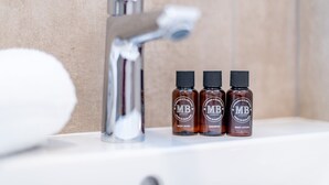 Un baño con grifo cromado y tres botellas de jabón corporal y loción sobre un estante blanco.