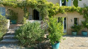 Un edificio de fachada de piedra, con varias ventanas con contraventanas y macetas con plantas.