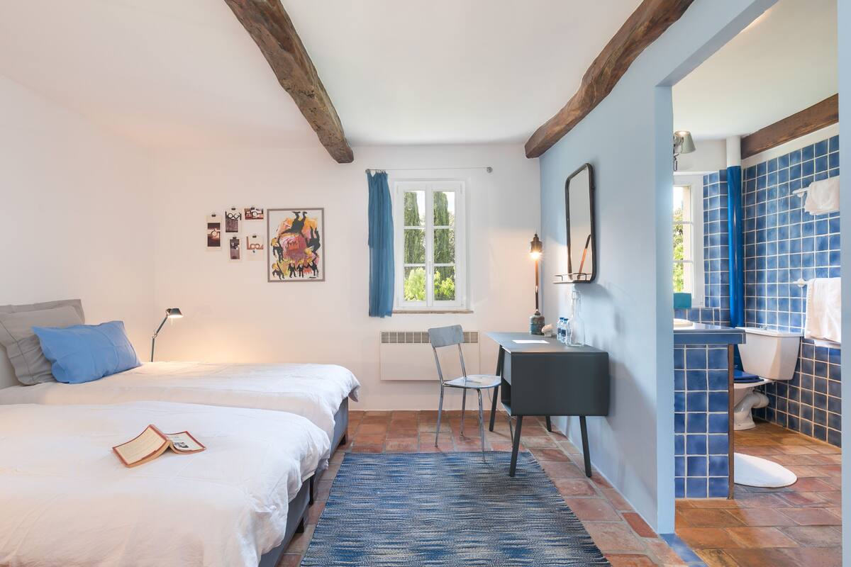 Ein Schlafzimmer mit Bett, Schreibtisch, Stuhl und einem Badezimmer mit blauen Fliesen.
