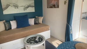 Un dormitorio moderno con un sofá, una mesita de noche con un reloj y una pared decorada con dos obras de arte.
