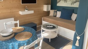 Una habitación acogedora con pared de madera, un sofá con cojines estampados, un televisor, una mesita y una silla.