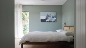 Ein Schlafzimmer mit einem Bett, einem Bild von zwei Personen am Strand und einem Fenster mit Vorhängen.