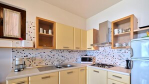 Una cocina con armarios color beige, salpicadero de azulejos, microondas, estufa y refrigerador.