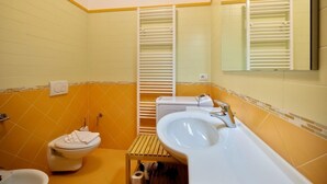 Un baño con azulejos amarillos y blancos, un inodoro, un lavabo y un espejo.