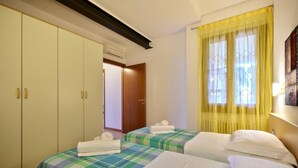 Habitación de hotel con dos camas, un armario y una ventana con cortinas amarillas.