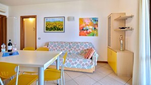 Una habitación con sofá, una mesa de comedor con sillas, un radiador y dos cuadros en la pared.