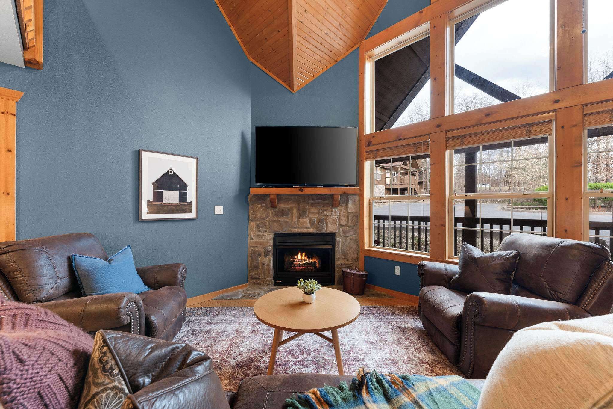 A living room with a stone fireplace, leather sofas, a television, and large windows.