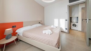 Een moderne hotelkamer met een bed, nachtkastje, lamp, wasmachine en een plafondlamp.