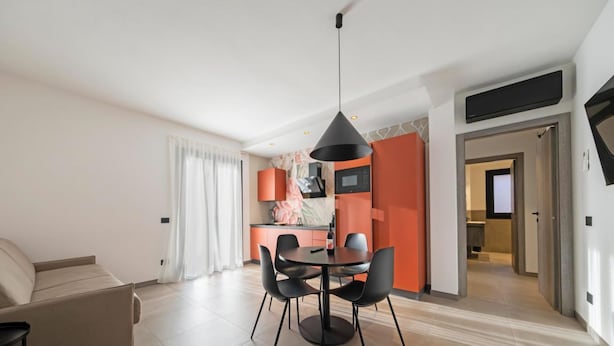 Een moderne woonkamer met een bank, eettafel en stoelen, een keuken met een magnetron, en een gang die naar een andere kamer leidt.