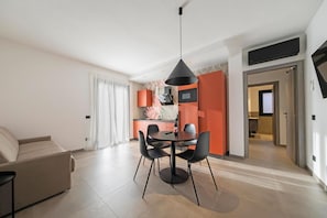 Ein modernes Wohnzimmer mit Sofa, Esstisch und Stühlen, eine Küche mit Mikrowelle sowie ein Flur, der in einen weiteren Raum führt.