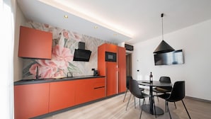 Een moderne keuken met oranje kastjes, een flatscreen televisie en een eetgedeelte met zwarte stoelen.