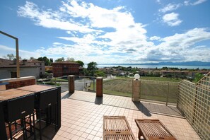 Eine Terrasse mit Blick auf einen See und ferne Berge, mit Tisch und Stühlen.