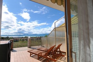 Un balcon avec vue sur la mer et les montagnes, un sol carrelé et des chaises en bois.