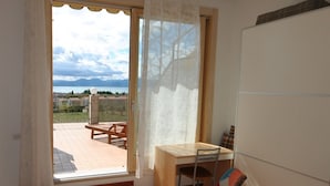 A room with a view of a body of water and mountains, a wooden table, a chair, and a sofa. - ApartmentsGarda - Rosa Chiarè (Bardolino)