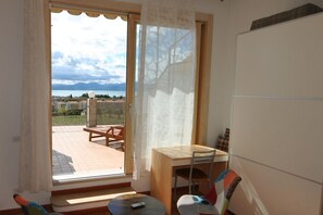 A room with a view of a body of water and mountains, a wooden table, a chair, and a sofa.
