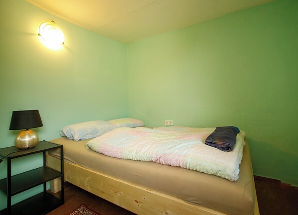 A single bed with a blanket, a bedside lamp, and a power outlet on the wall. - Monteurshaus im Leipziger Süde Nähe A38 (Leipzig)
