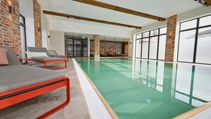 Una piscina interior con diseño moderno, que cuenta con una zona de estar con marco rojo y grandes ventanales.
