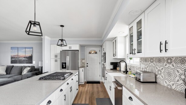 Une cuisine moderne avec des meubles blancs, un îlot central, un réfrigérateur et un grille-pain.