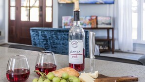 Un comptoir de cuisine avec une bouteille de vin rouge, deux verres, une planche à découper en bois avec des raisins et du fromage, et un couteau.