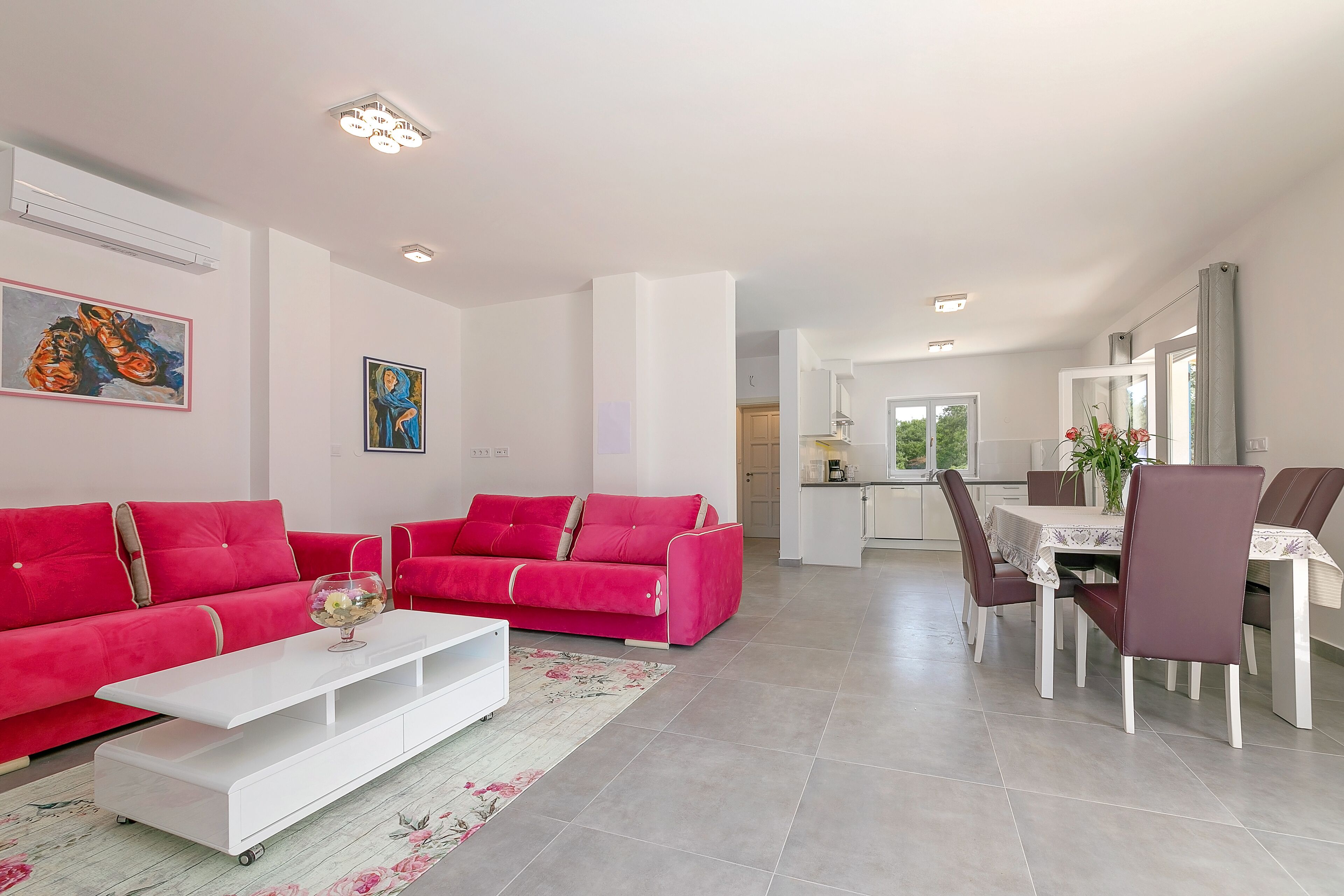 A modern living room with a red sofa set, a white coffee table, and a dining area with a table and chairs.