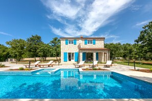 Un bâtiment en pierre avec des volets bleus, une piscine et des chaises longues.