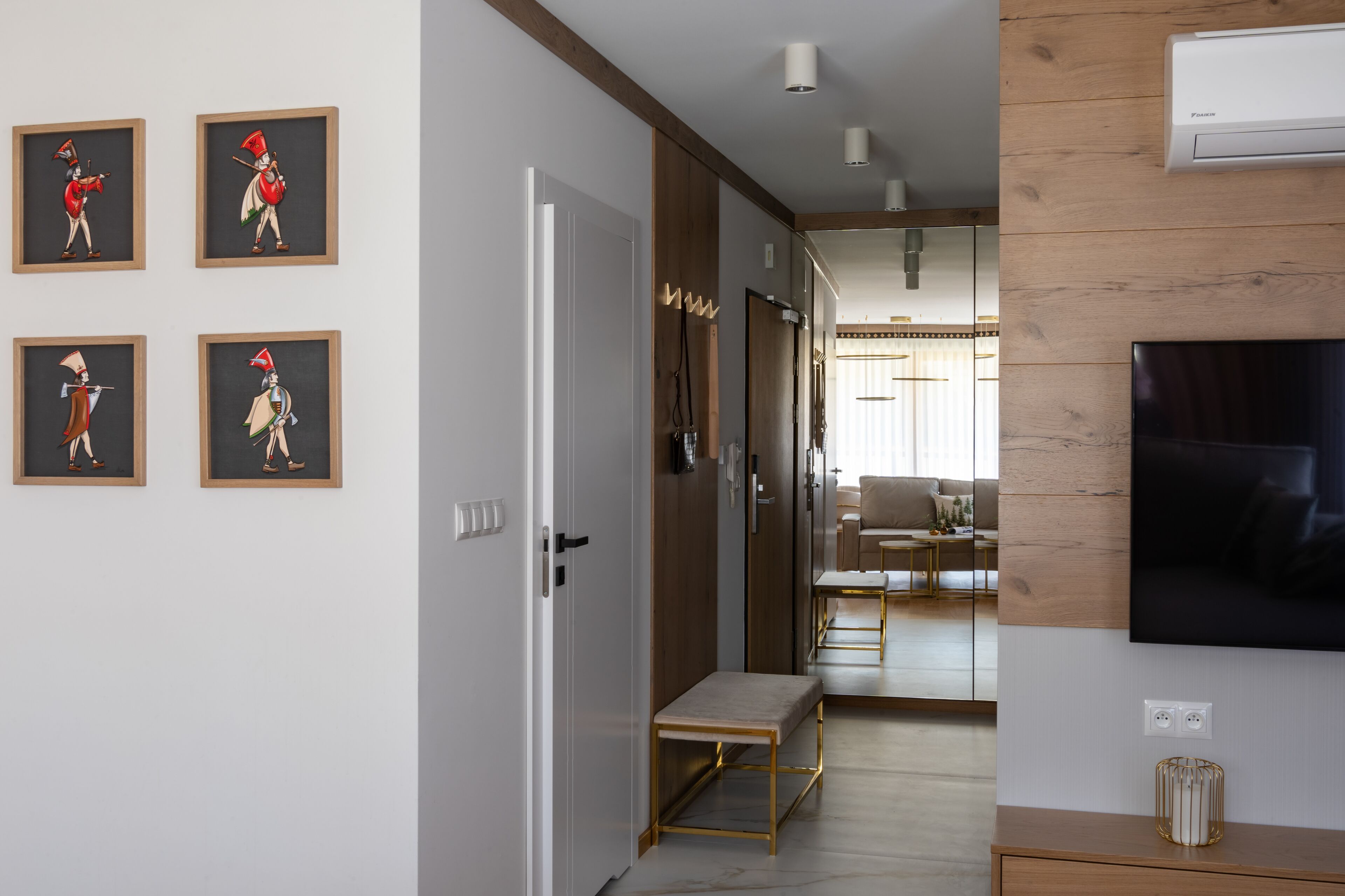 A modern living room with a flat-screen TV, wooden paneling, a bench, and framed artwork on the wall.