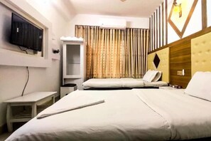 A hotel room with a bed, a bedside table, a TV mounted on the wall, and a window with curtains. - White Rose Suites Ltd (Dhaka)