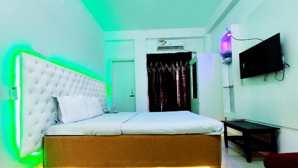 A bedroom with a large bed, an air conditioning unit, a TV mounted on the wall, and a bedside table. - White Rose Suites Ltd (Dhaka)