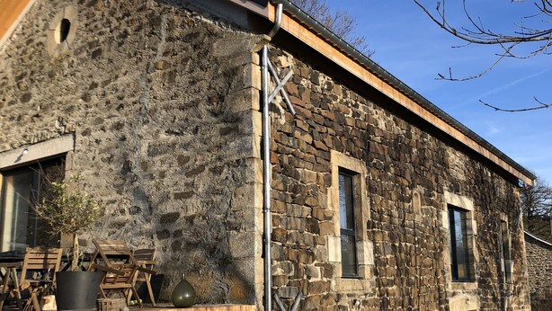 Un edificio de piedra con una terraza de madera, una estructura metálica en forma de X y un camino de entrada de grava.