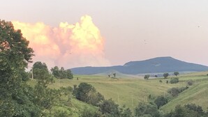 Un paisaje con colinas ondulantes, árboles dispersos y una colina destacada al fondo.