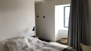 Un dormitorio con cama, lámpara, ventana con cortinas y una cesta pequeña.