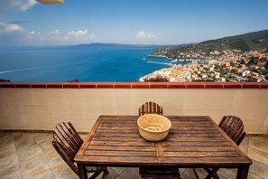 A wooden table and chairs on a balcony with a view of the sea and a coastal town.
