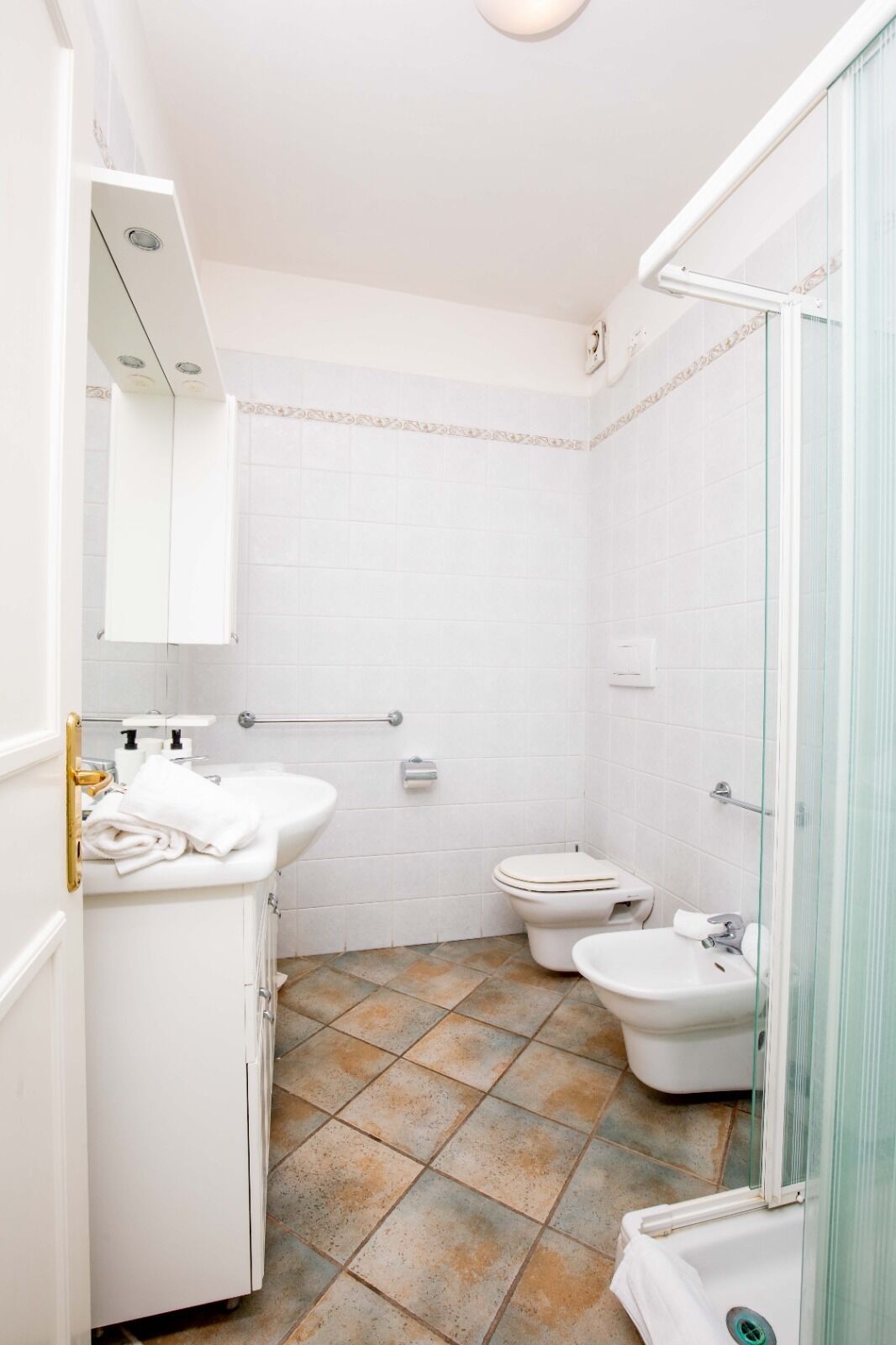 A bathroom with white tiles, a sink, a toilet, and a bidet.