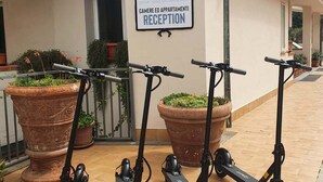Zona de recepción con un cartel que indica que pertenece a un alojamiento turístico residencial. Hay tres patinetes eléctricos estacionados adelante.