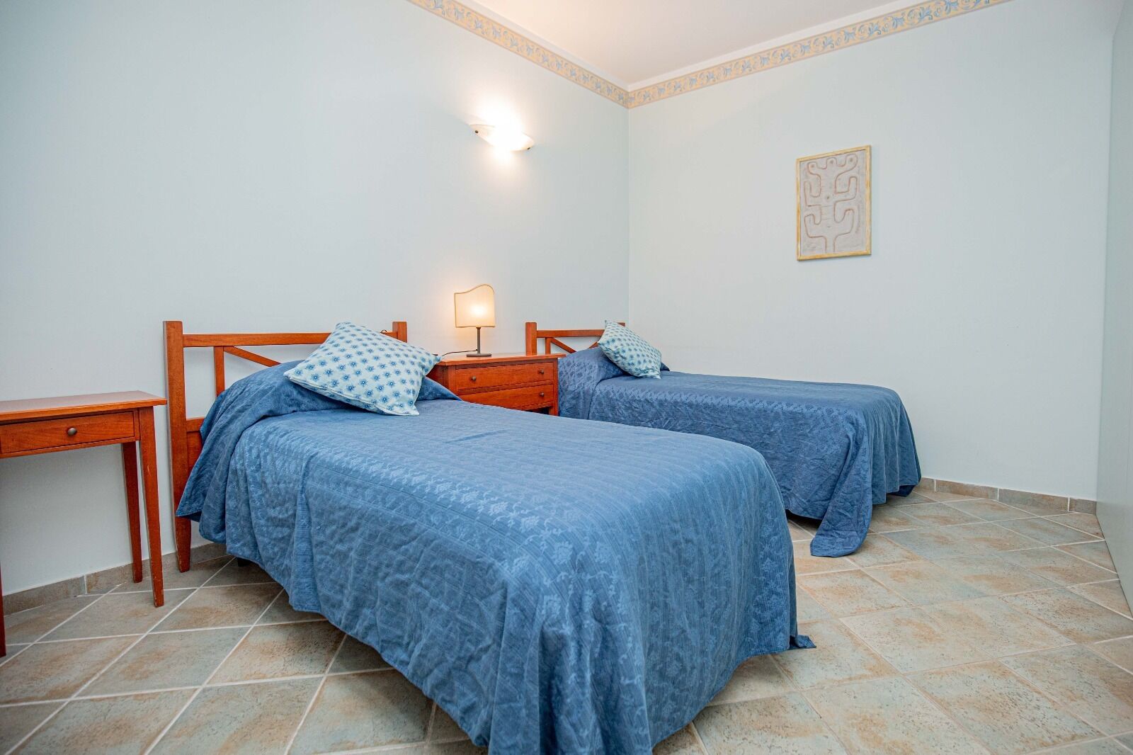 A room with two beds, a nightstand, a lamp, and a small table.